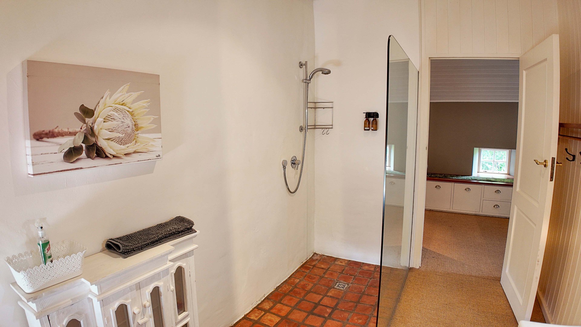 Bathroom with glass shower, protea artwork and terracotta floor