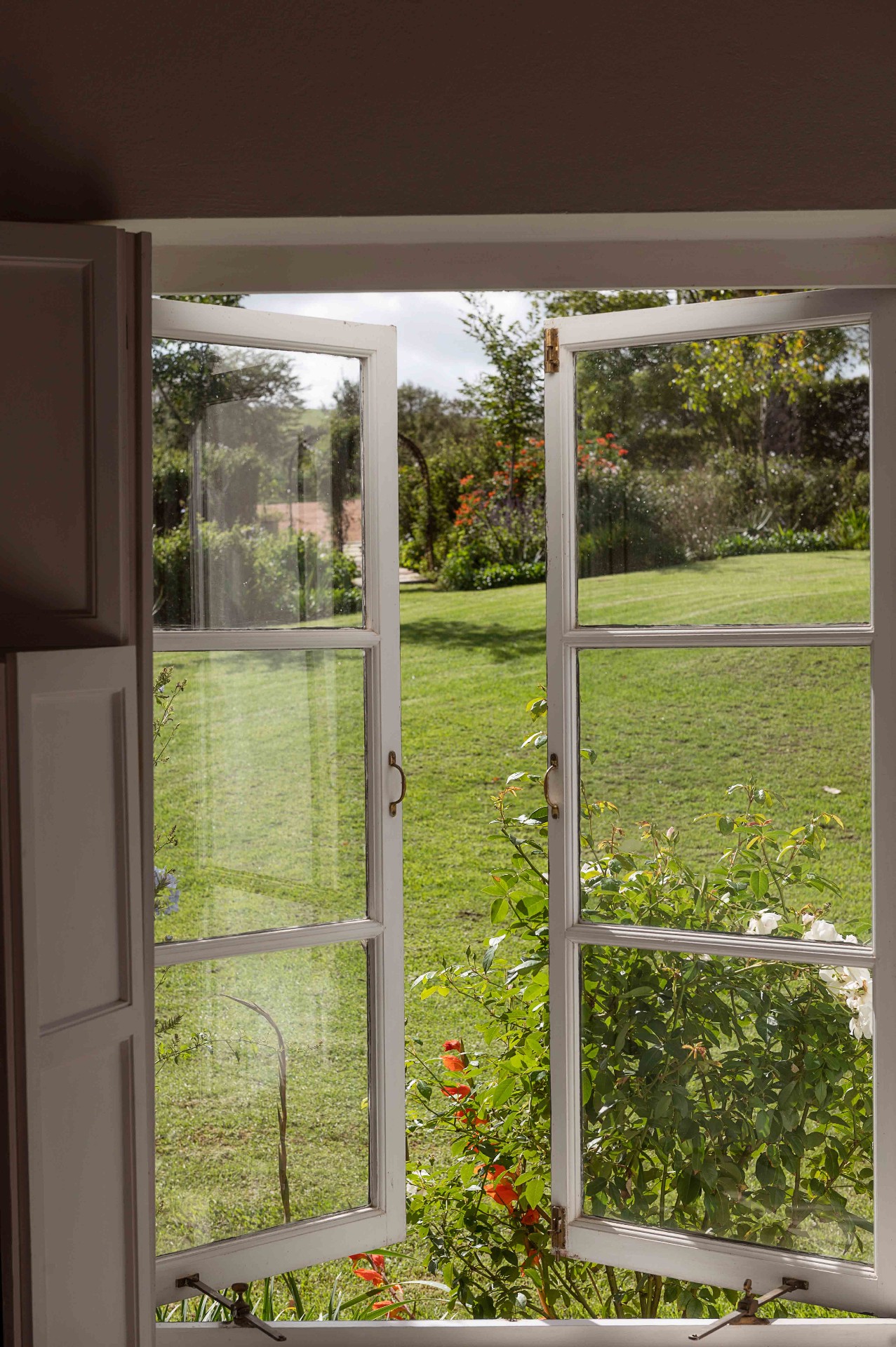 Open casement window framing the rose garden and lawn