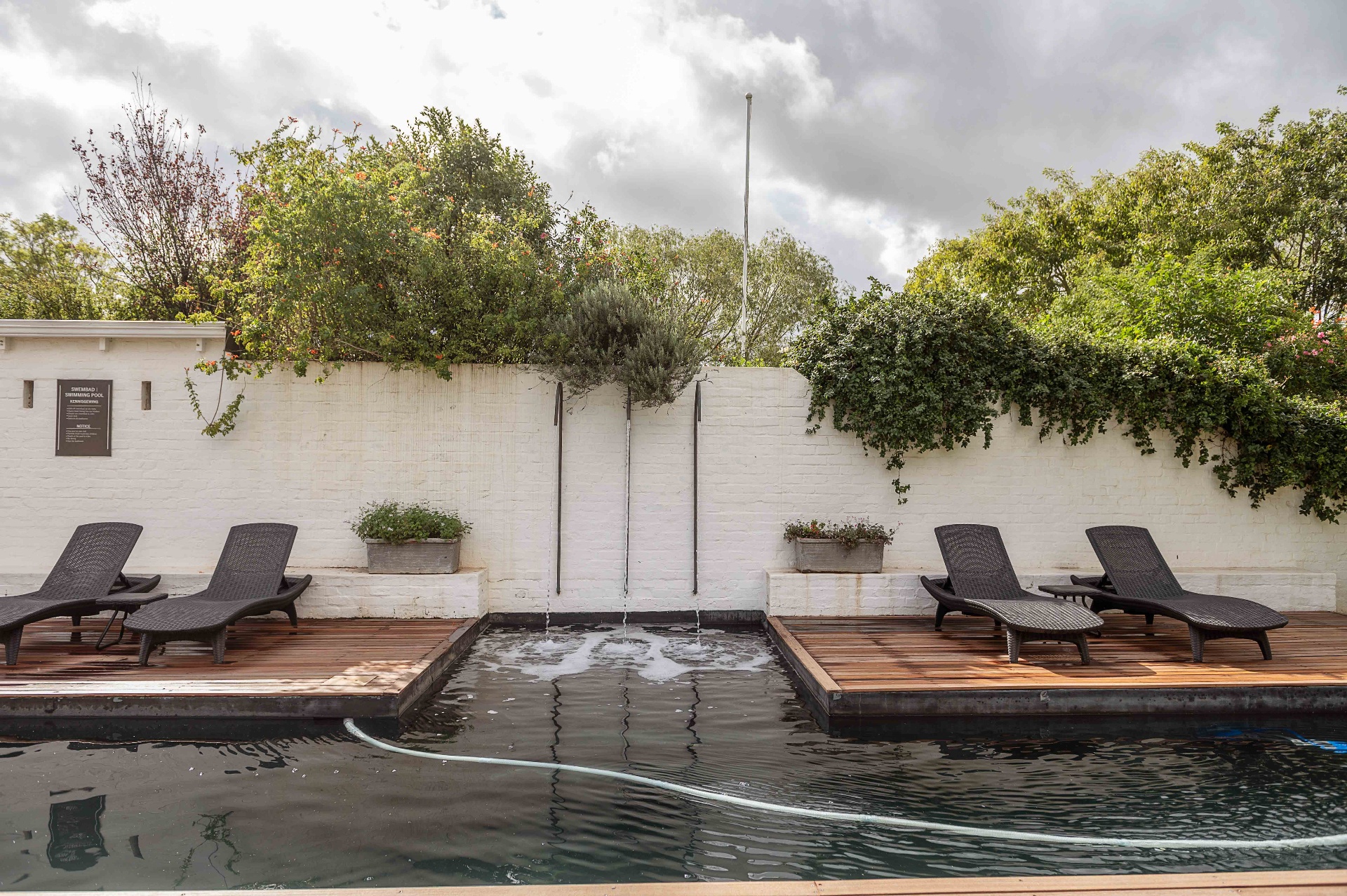 Poolside loungers along whitewashed wall with fountain spouts