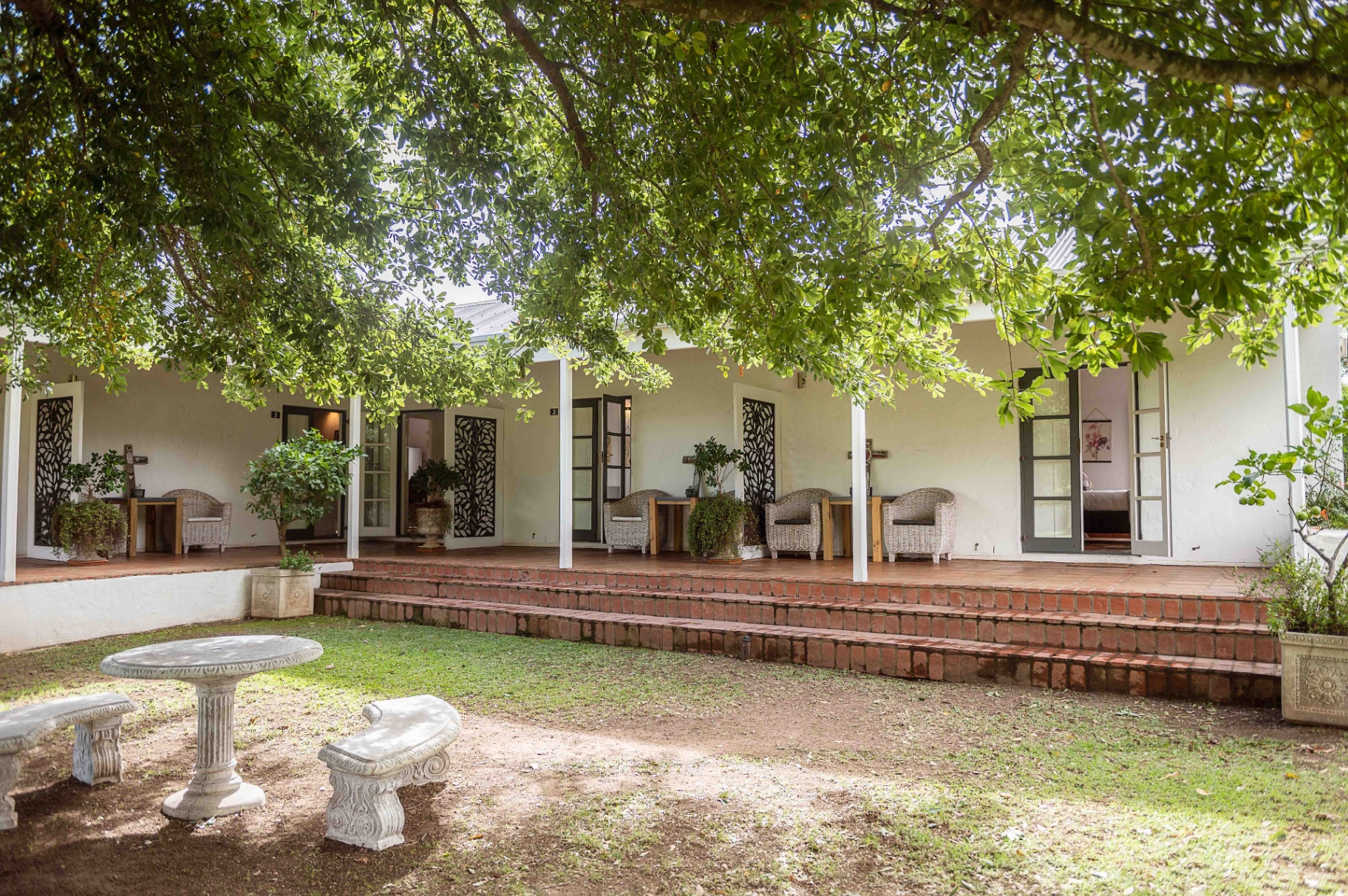 Tree-shaded porch with wicker chairs and brick steps